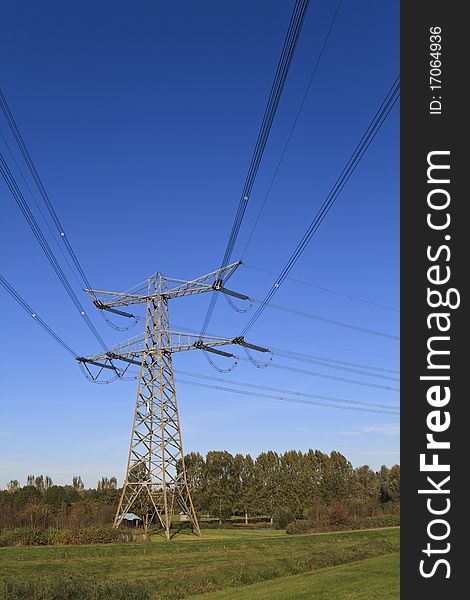 Electricity pylon in perspective against a deep blue sky standing in a green field. Electricity pylon in perspective against a deep blue sky standing in a green field