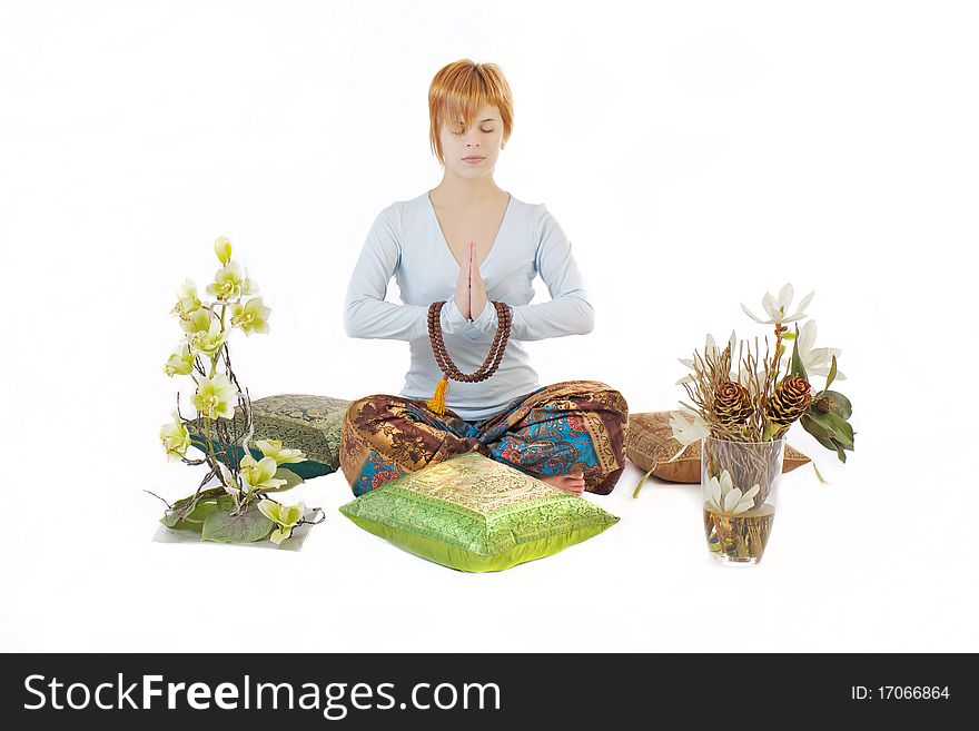 The girl meditates with eyes closed among the pillows and lotus flowers and orchids on a white background. The girl meditates with eyes closed among the pillows and lotus flowers and orchids on a white background.