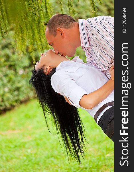 Young man kissing woman in th neck couple kissing in the park. Young man kissing woman in th neck couple kissing in the park