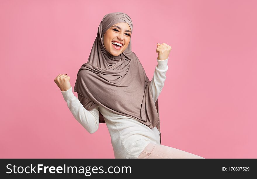 Yes. Happy muslim woman in hijab rejoicing success, raising hands and exclaiming with winner face expression. Yes. Happy muslim woman in hijab rejoicing success, raising hands and exclaiming with winner face expression