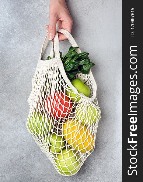 Zero Waste Eco Mesh Shopping Bag With Fruits Vegetables Greens On Grey Concrete Background. Hand Holding Eco Friendly Bag