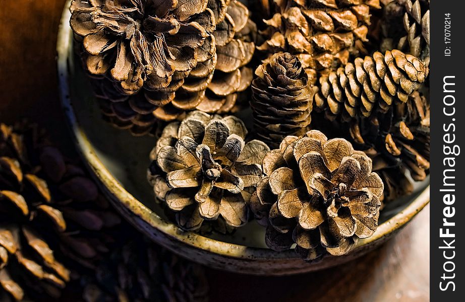 A pottery bowl filled with pine cones and sitting on a wooden table indoors. A pottery bowl filled with pine cones and sitting on a wooden table indoors.