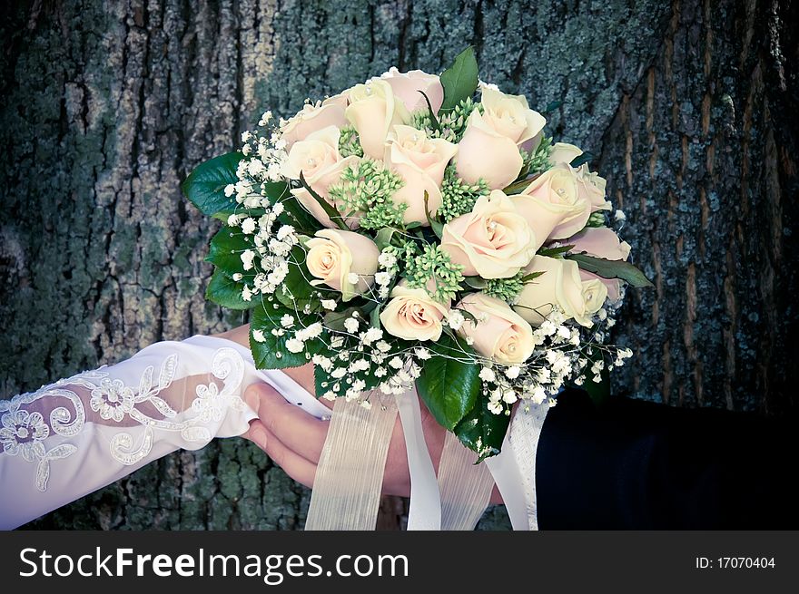 Hands of the newlyweds holding a bouquet of roses
