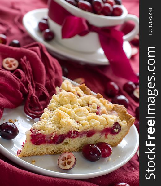 Piece of cranberry cake with cup of cranberry on background