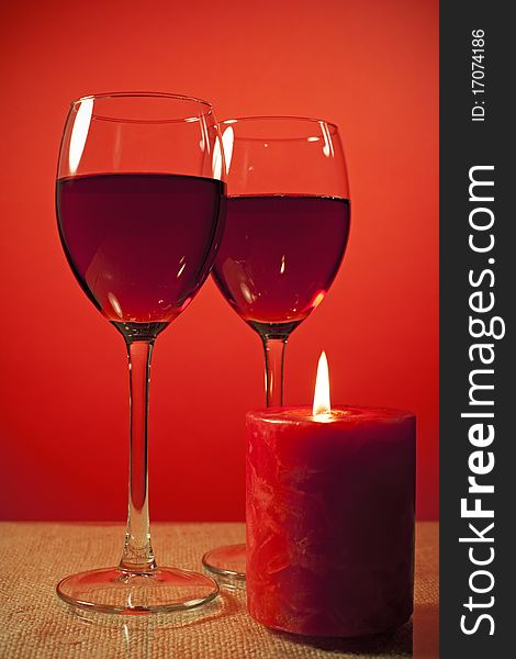 Two Glass of wine and a candle over red background