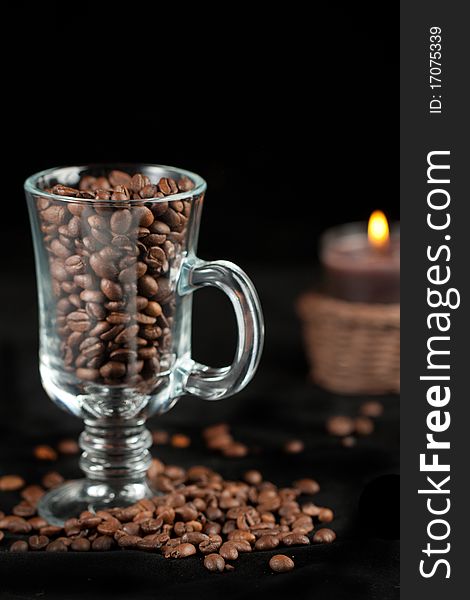 Fragrant fried coffee beans in the glass and burning candle over black. Fragrant fried coffee beans in the glass and burning candle over black