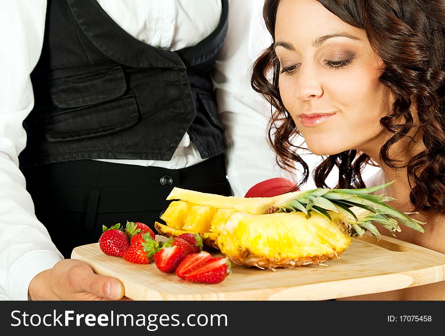 Female looking at fresh sliced strawberries and pineapple on cutting board held by waitress. Female looking at fresh sliced strawberries and pineapple on cutting board held by waitress