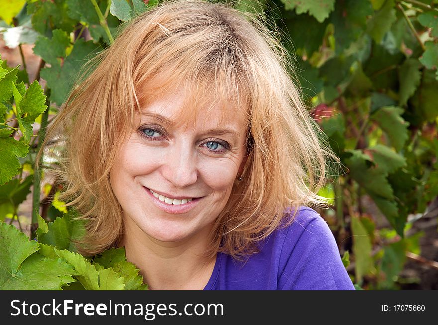 Blue-eyed woman in a blue shirt on the background of vine leaves. tousled blond hair.