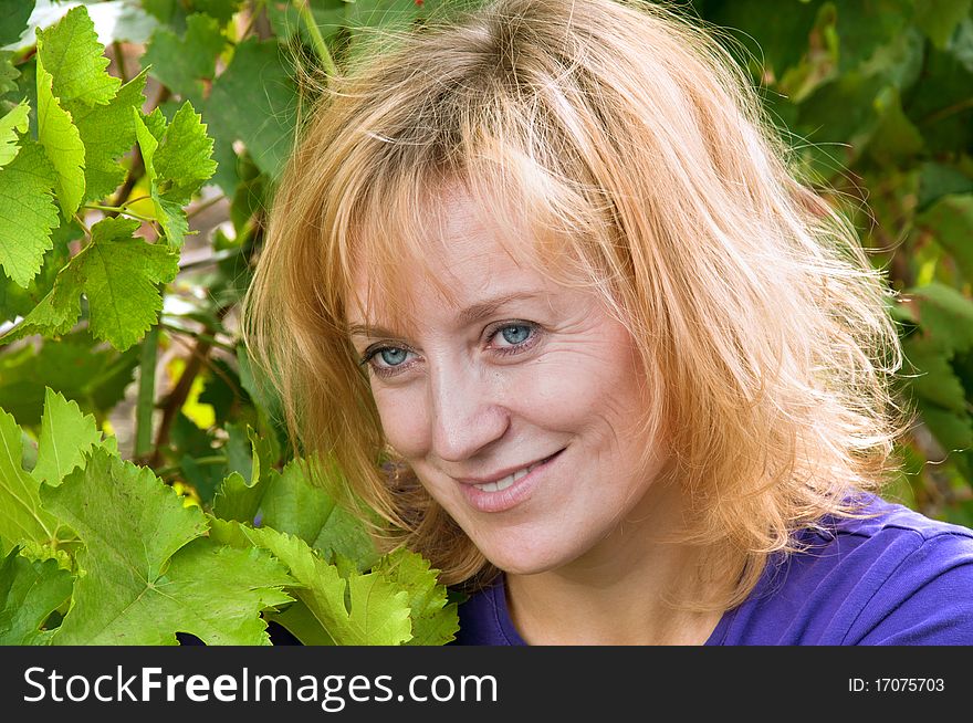 Blue-eyed woman in a blue shirt on the background of vine leaves. tousled blond hair.