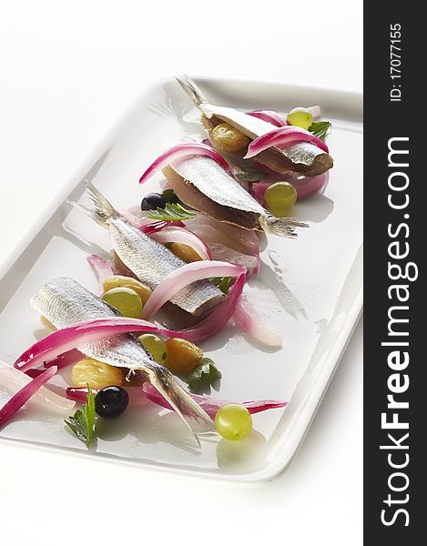Sardines with grapes and red onion on white plate