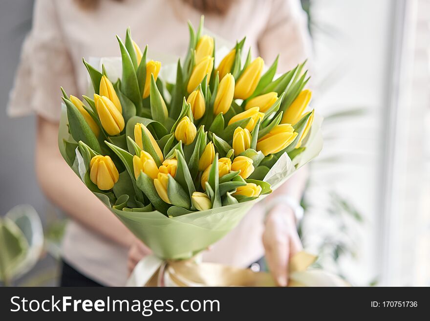 Young beautiful woman holding a spring bouquet of yellow tulips in her hand. Bunch of fresh cut spring flowers in female hands.