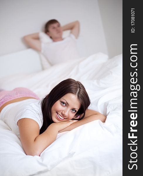 Happy young woman and  sleeping man on the bed at home (focus on the woman). Happy young woman and  sleeping man on the bed at home (focus on the woman)