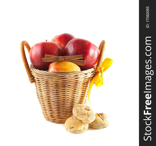 Red apples in a basket with cookies and cinnamon. Isolated on white background