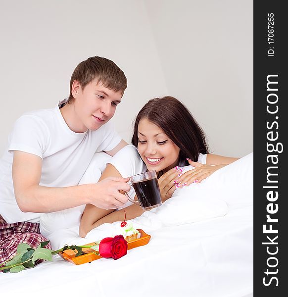 Young man bringing his girlfriend a rose and coffee in bed