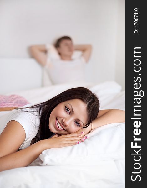 Happy young woman and  sleeping man on the bed at home (focus on the woman). Happy young woman and  sleeping man on the bed at home (focus on the woman)