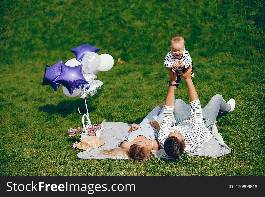 A young and beautiful blonde mother in a blue dress, along with her handsome men dressed in a white jacket, sitting with her little son in the summer solar park. A young and beautiful blonde mother in a blue dress, along with her handsome men dressed in a white jacket, sitting with her little son in the summer solar park