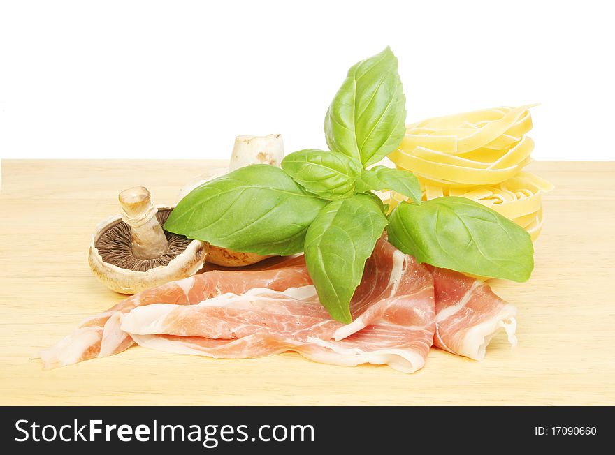 Fresh basil herb leaves,mushrooms, parma ham and tagliatelle on a wooden board. Fresh basil herb leaves,mushrooms, parma ham and tagliatelle on a wooden board