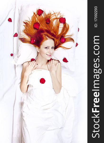 Beautiful red-haired girl in bed with rose petal. Studio shot.