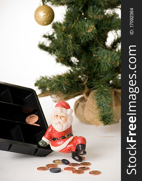 A vertical image of a santa clause ornament sitting on the edge of a coin box with only a few pennies and two buttons, suggesting low funds at christmas. A vertical image of a santa clause ornament sitting on the edge of a coin box with only a few pennies and two buttons, suggesting low funds at christmas