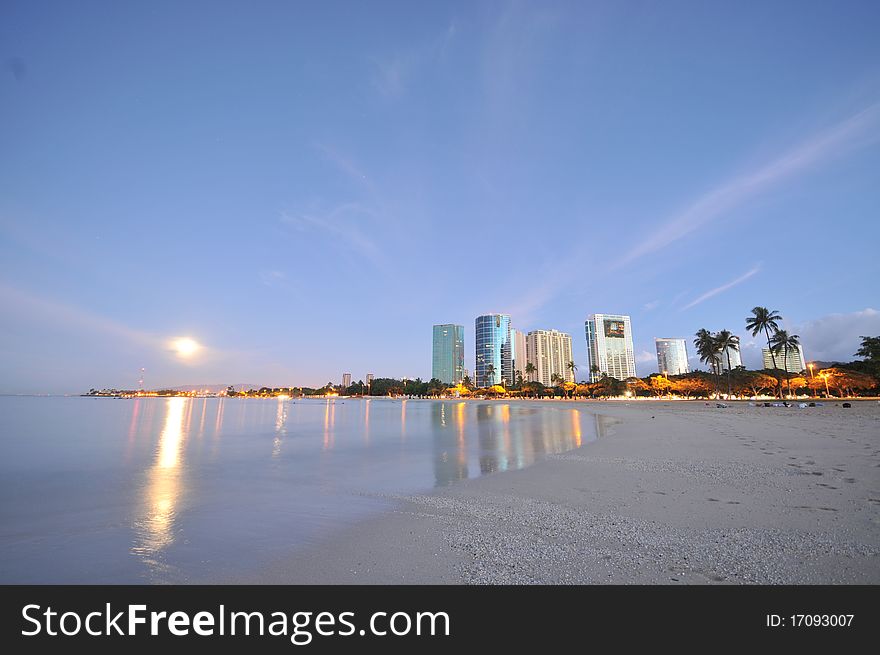 Buildings and ocean with a full moon setting. Buildings and ocean with a full moon setting.