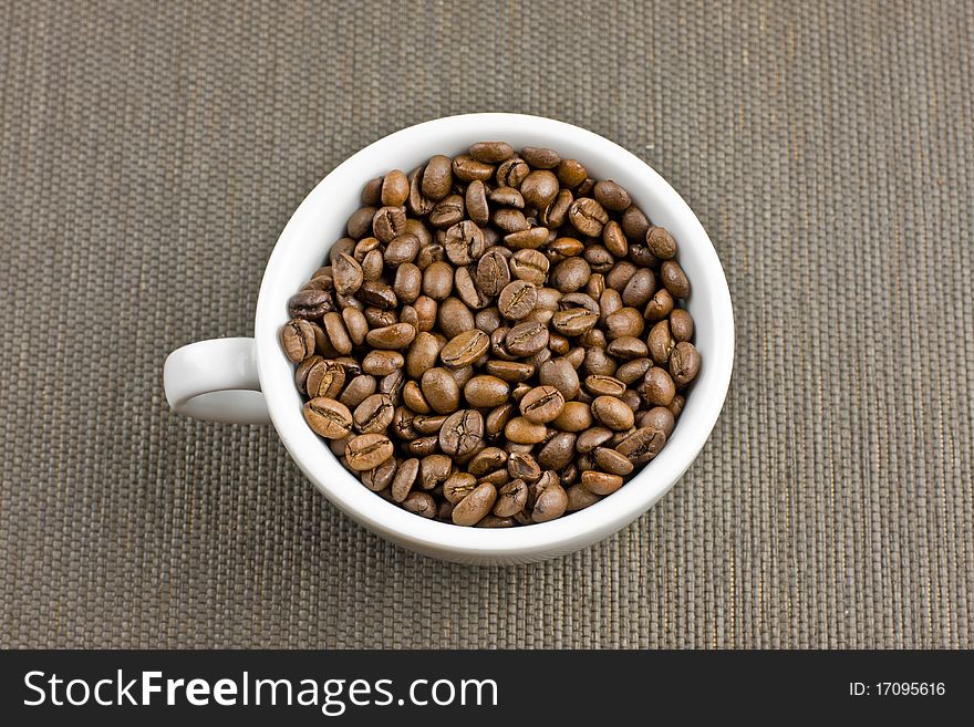 Big coffee cup full with coffee beans in the middle of the table with grey backround. Big coffee cup full with coffee beans in the middle of the table with grey backround