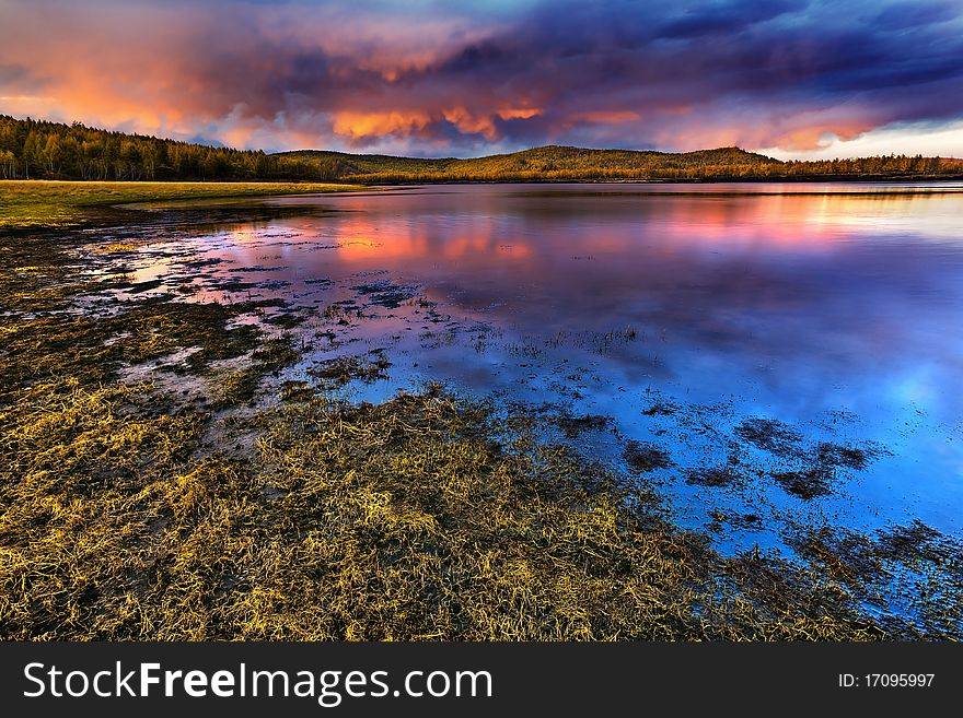 This is a picture of the sunset under the lake and forest.