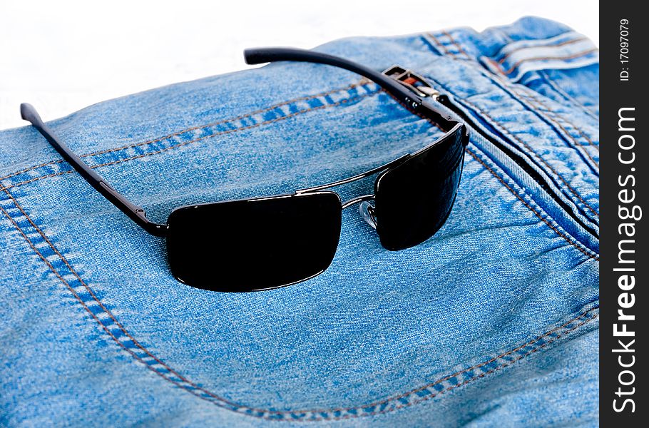 Sunglasses resting upon jeans on white background. Sunglasses resting upon jeans on white background