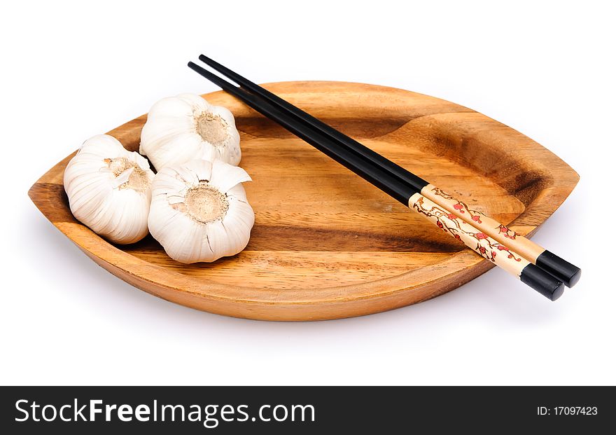 Two chop sticks and some garlic on a wooden plate. Two chop sticks and some garlic on a wooden plate