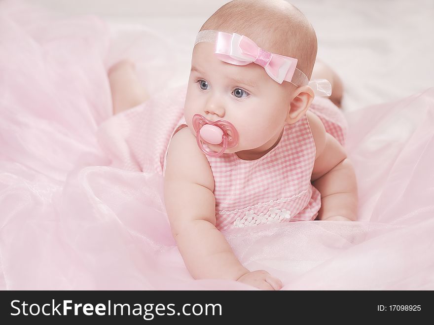 Portrait of a little baby on a soft blanket with a pacifier and pink bow