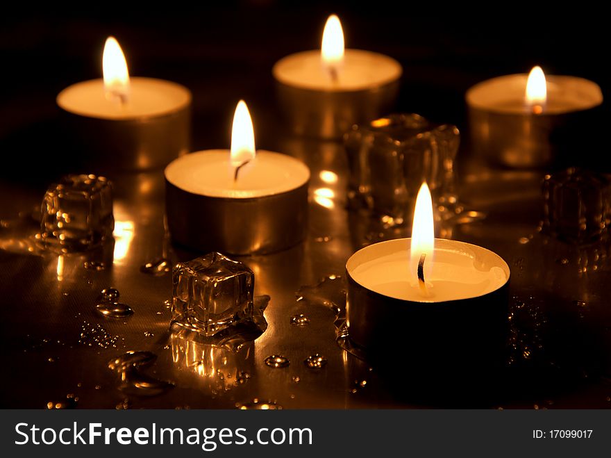 Five lighted candles with melting ice cubes and water drops