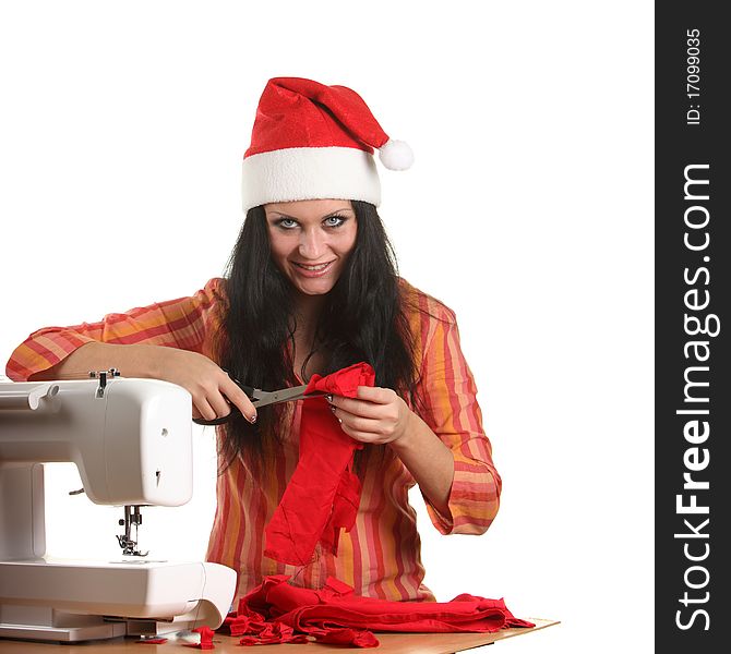 Beautiful woman seamstress in a Christmas hat cut red cloth by scissors. Beautiful woman seamstress in a Christmas hat cut red cloth by scissors