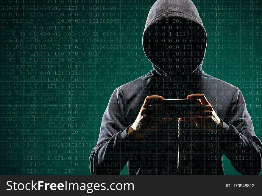 Anonymous computer hacker with a smartphone over abstract digital background. Obscured dark face in mask and hood. Data thief, internet attack, darknet fraud, dangerous viruses and cyber security concept.