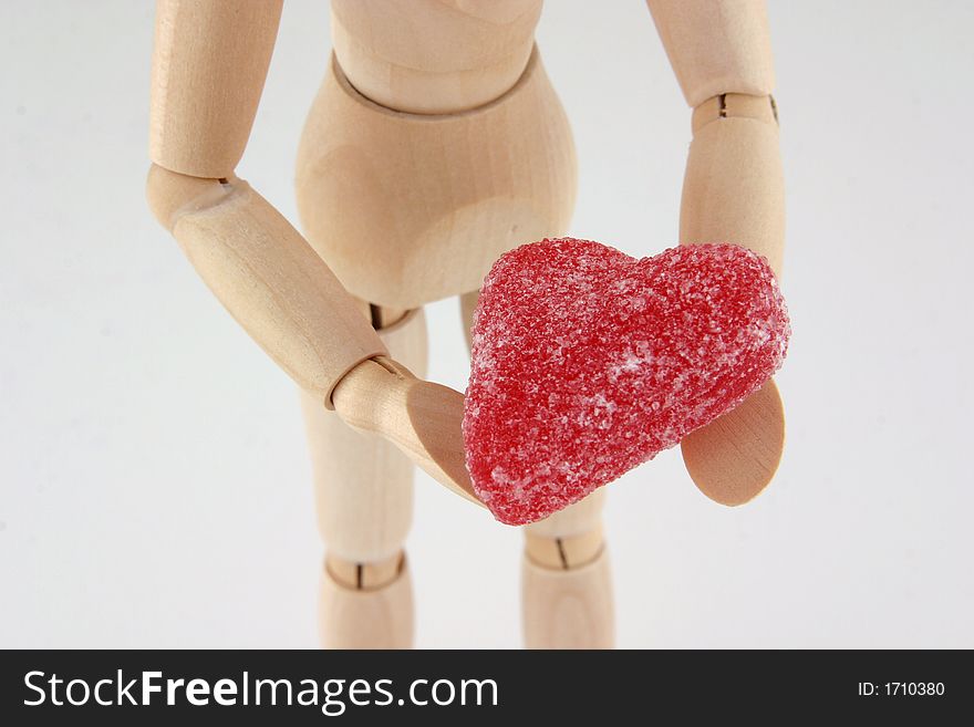 Closeup selective focus image of a wood manikin holding a red heart shaped candy. Closeup selective focus image of a wood manikin holding a red heart shaped candy.