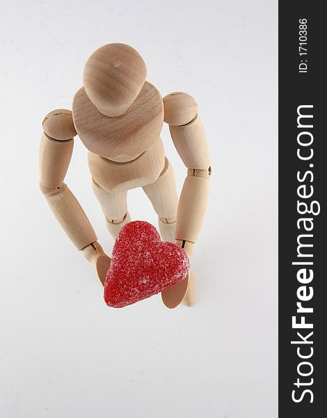 Selective focus top view image of a wood manikin holding a red heart shaped candy. Selective focus top view image of a wood manikin holding a red heart shaped candy.