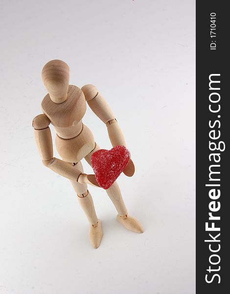 Selective focus image from above of a wood manikin holding a red heart shaped candy. Selective focus image from above of a wood manikin holding a red heart shaped candy.