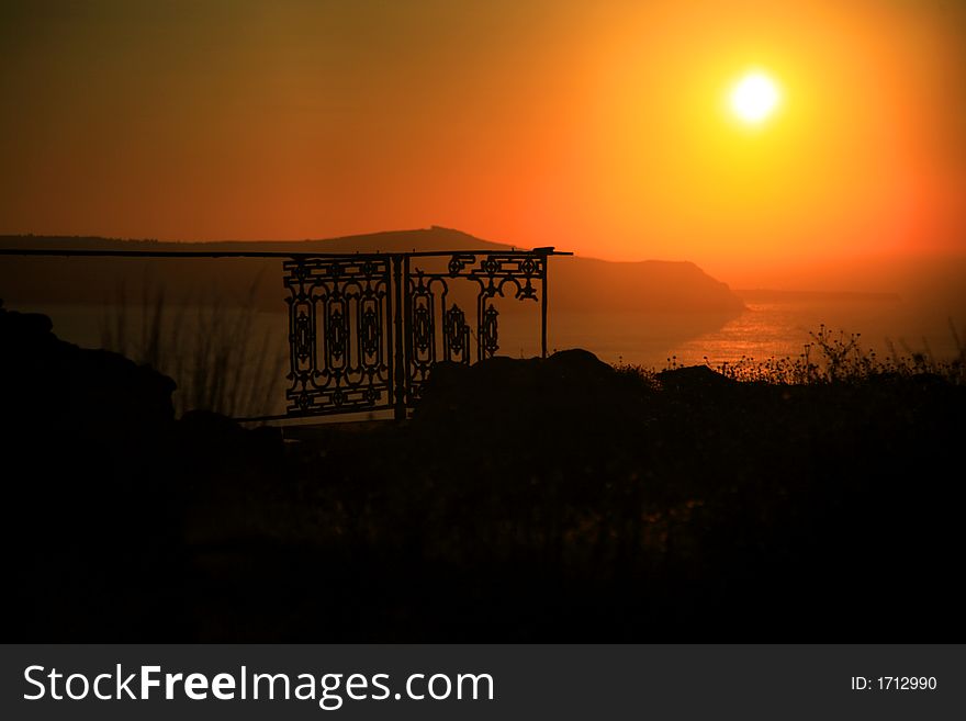 Sun setting across the sea Oia Santorini with old railings silhouetted in the foreground. Sun setting across the sea Oia Santorini with old railings silhouetted in the foreground