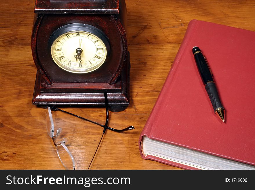 This is an image of a clock and book on a wooden desktop. This is an image of a clock and book on a wooden desktop.