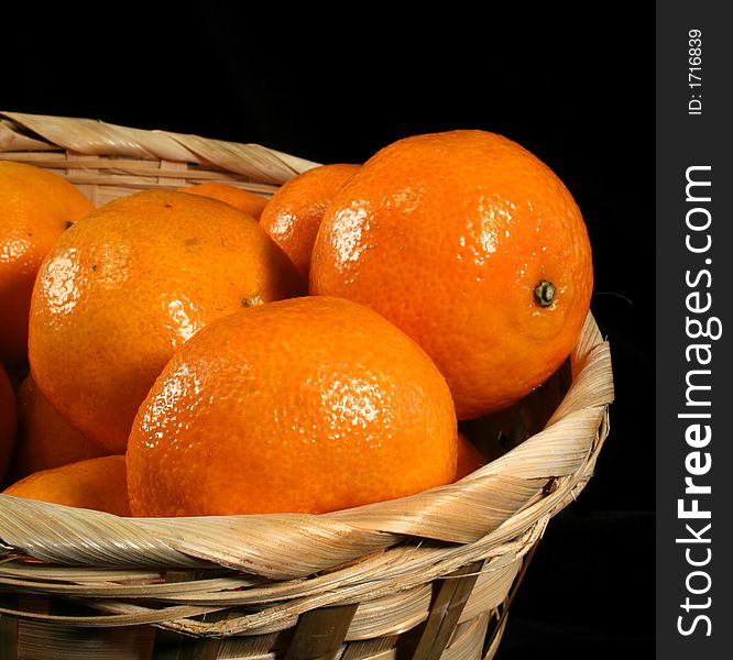 Clementines imported from Spain in a basket on a black background.  These are also knows as Satsumas and are grown in southern Louisiana.