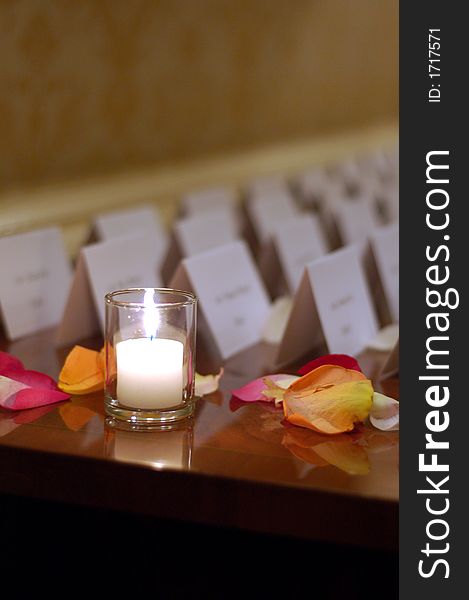 Candle and flower petals on a desk next to rows of name tags for guests. Candle and flower petals on a desk next to rows of name tags for guests.