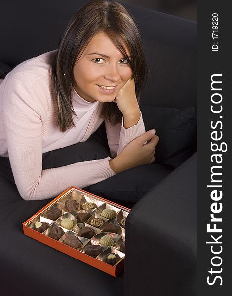 Young woman lying on the black sofa with box of chocolates. Young woman lying on the black sofa with box of chocolates.