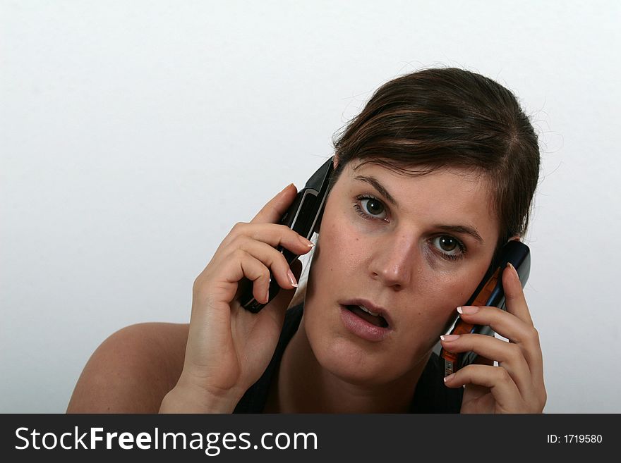 A young woman speaking on two phones being stressed.