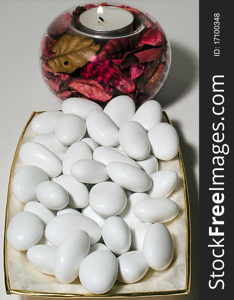 A plate filled with sugared almonds and a lighted wax candle. A plate filled with sugared almonds and a lighted wax candle