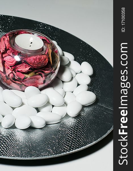 A round plate filled with sugared almonds and a lighted wax candle. A round plate filled with sugared almonds and a lighted wax candle