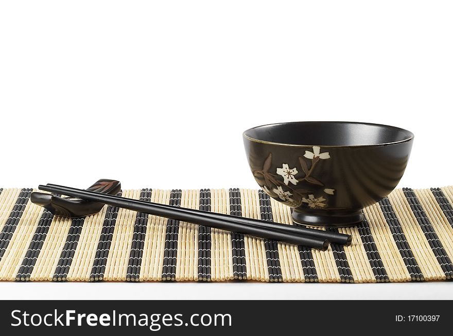 Wooden chopsticks and little ceramic bowl on the bamboo mat over white background. Wooden chopsticks and little ceramic bowl on the bamboo mat over white background