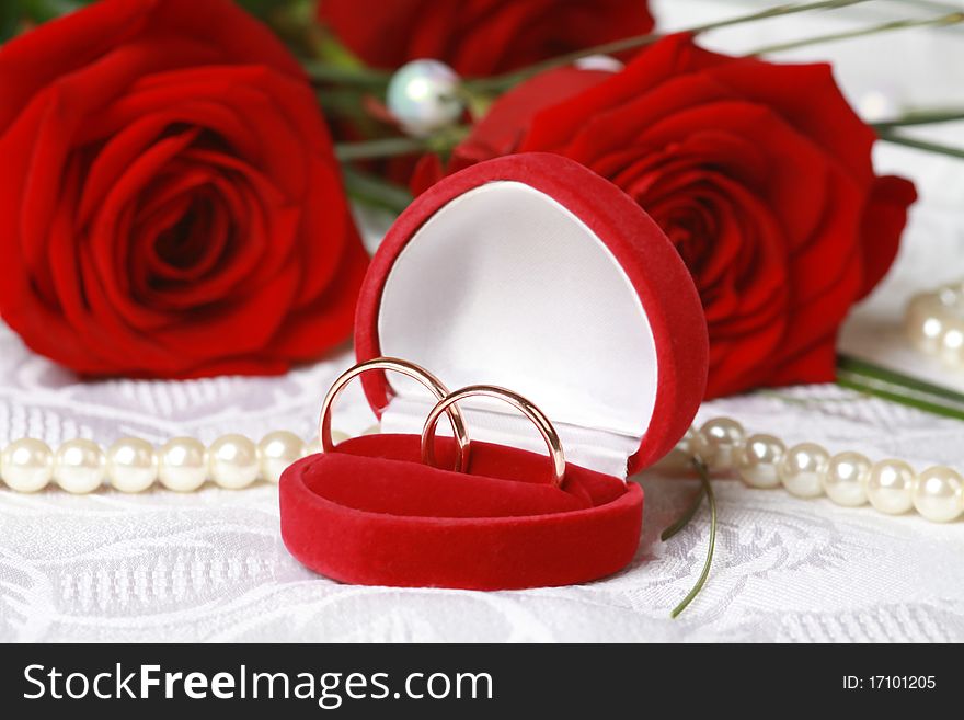 Wedding rings in red box against beautiful red roses on lace background