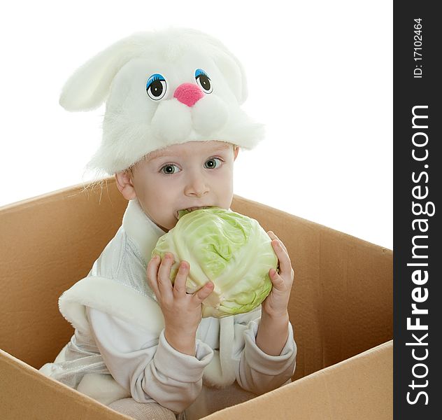 The boy in a suit of a rabbit sits in a box and holds cabbage