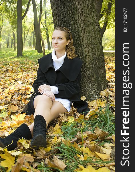 Pensive teen girl sits under the tree among gold leaves in autumn park. Pensive teen girl sits under the tree among gold leaves in autumn park