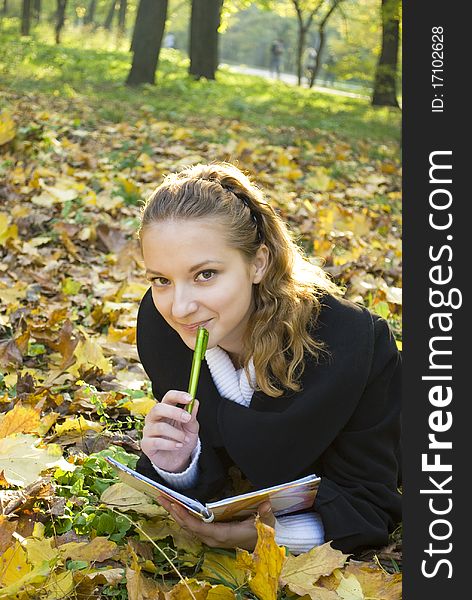 Teen girl lies in gold autumn park with her diary