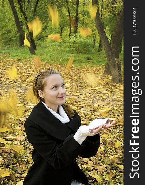 Happy teen girl catches leaves in autumn park
