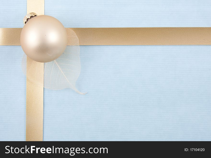 Christmas back ground with gold ribbon on light blue paper with a golden ball on a leaf at the left. Christmas back ground with gold ribbon on light blue paper with a golden ball on a leaf at the left